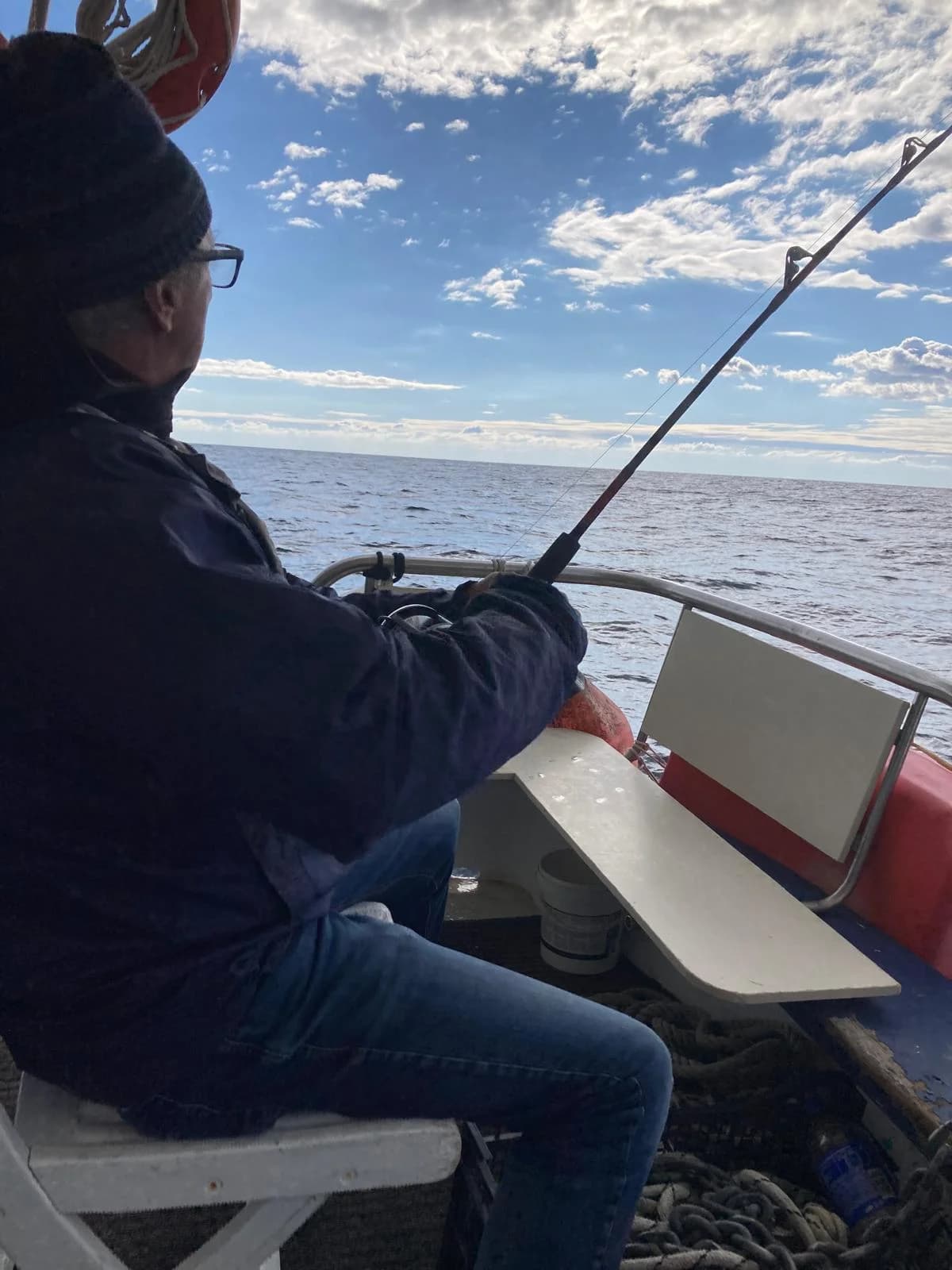 An adult guest fishing from the boat under a bright Aegean sky